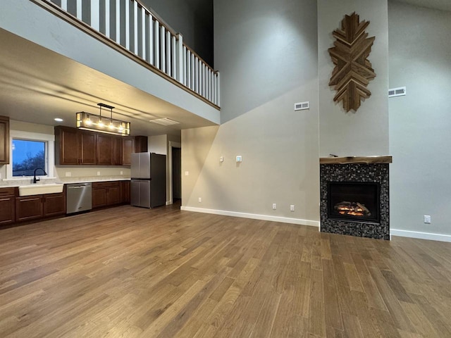 unfurnished living room with a high ceiling, light hardwood / wood-style flooring, a tiled fireplace, and sink