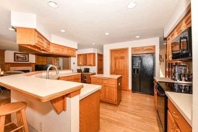 kitchen featuring a kitchen breakfast bar, a center island, black appliances, and light hardwood / wood-style floors