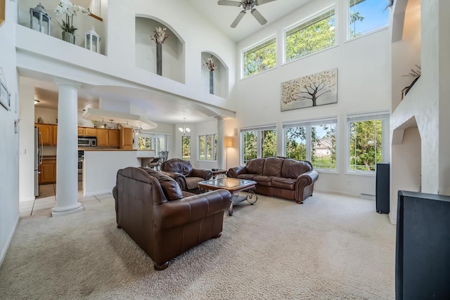 living room featuring ornate columns, ceiling fan with notable chandelier, light colored carpet, and a high ceiling