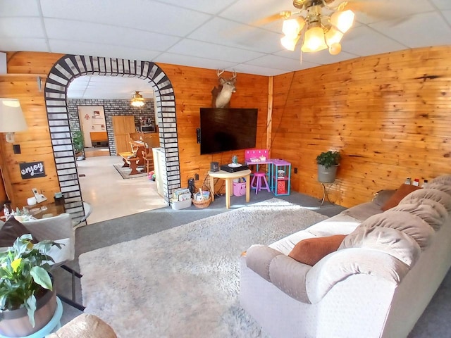 living room featuring ceiling fan, wood walls, a drop ceiling, and concrete flooring