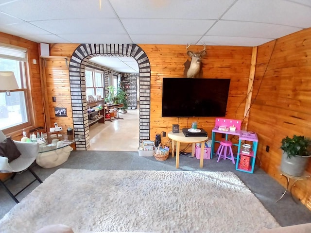 living room featuring wooden walls, a drop ceiling, and concrete flooring