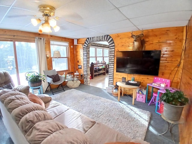 living room with a paneled ceiling, wooden walls, and ceiling fan