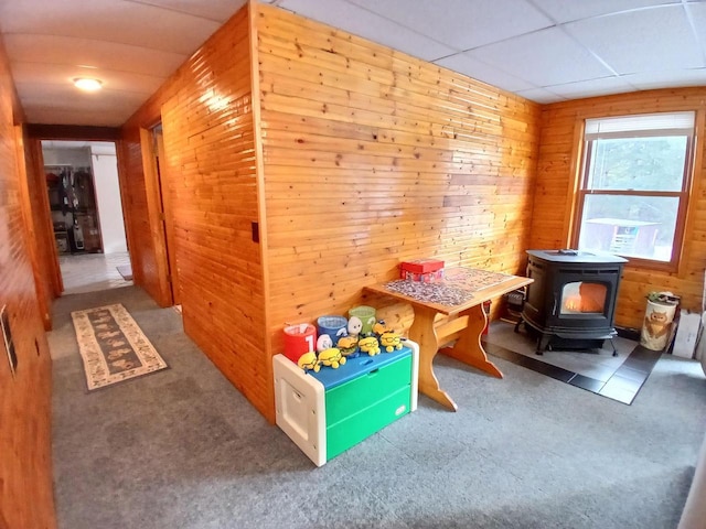 game room featuring a wood stove, a drop ceiling, and wood walls