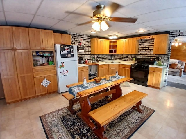 kitchen with a paneled ceiling, black range oven, brick wall, and white refrigerator