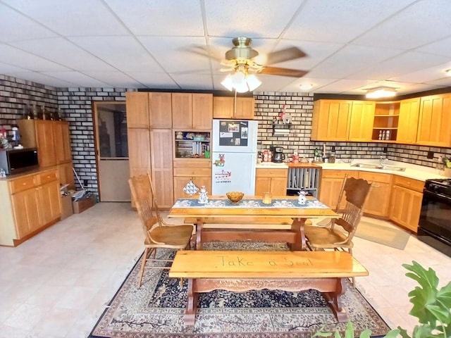 dining room with a drop ceiling, ceiling fan, sink, and brick wall