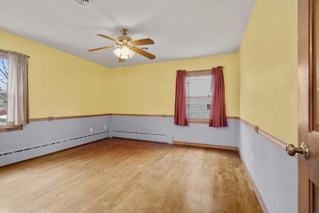 empty room featuring hardwood / wood-style floors, ceiling fan, and a baseboard heating unit