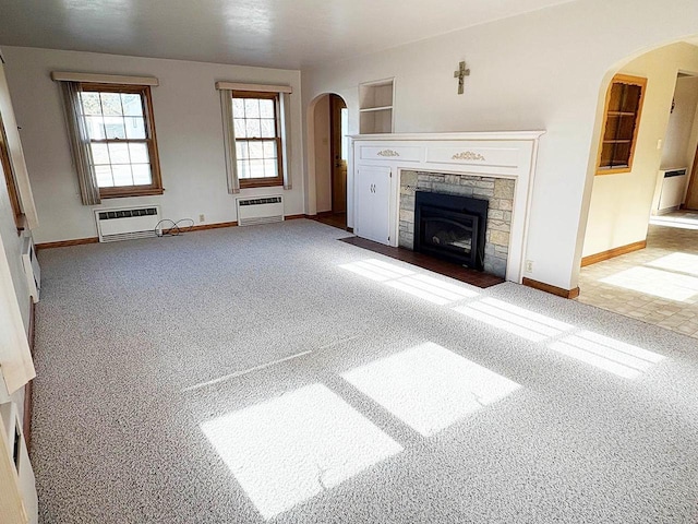 unfurnished living room with a wall mounted air conditioner, light colored carpet, a stone fireplace, and built in features