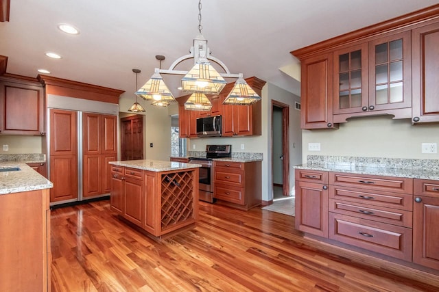 kitchen with dark wood-type flooring, hanging light fixtures, a kitchen island, light stone counters, and stainless steel appliances