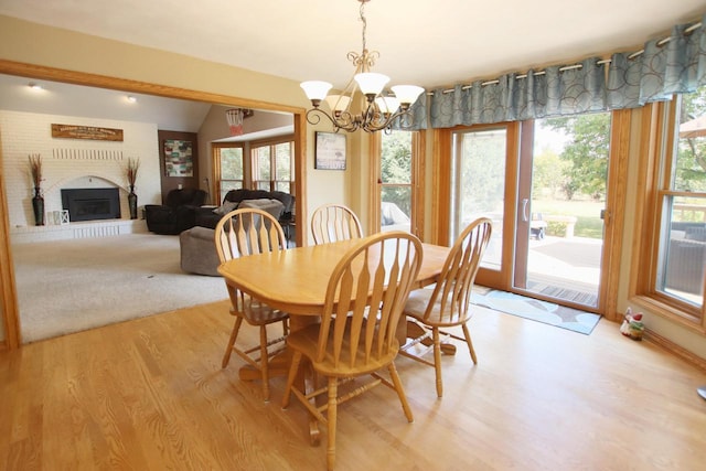 dining area with light hardwood / wood-style flooring, lofted ceiling, a fireplace, and an inviting chandelier