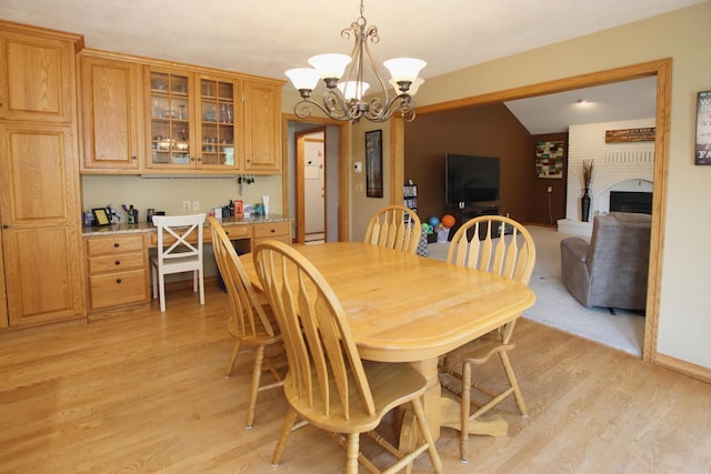 dining room featuring a large fireplace, lofted ceiling, light hardwood / wood-style flooring, and an inviting chandelier