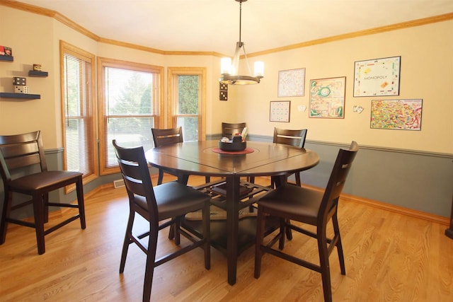 dining space with light hardwood / wood-style floors, ornamental molding, and an inviting chandelier