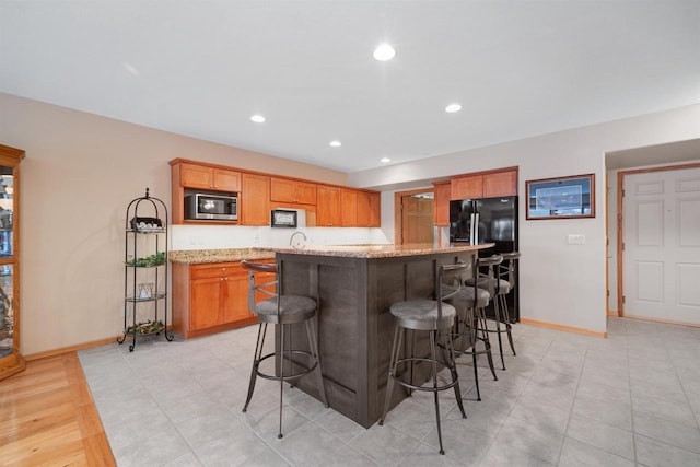 kitchen with stainless steel microwave, a center island, black fridge, light stone countertops, and a breakfast bar area