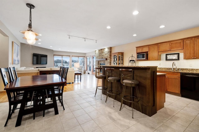 kitchen with light stone countertops, track lighting, black dishwasher, a kitchen breakfast bar, and hanging light fixtures