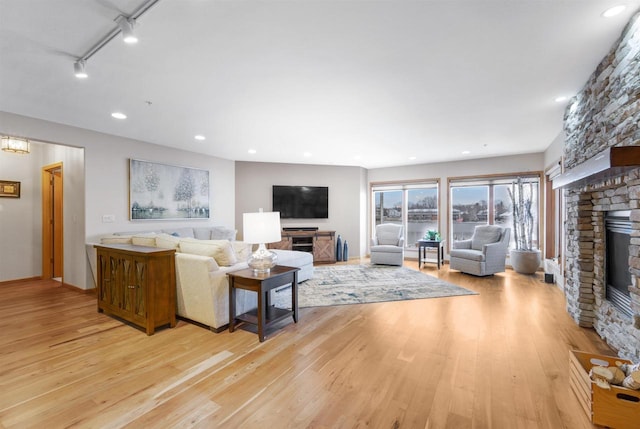 living room featuring a stone fireplace, light hardwood / wood-style floors, and rail lighting