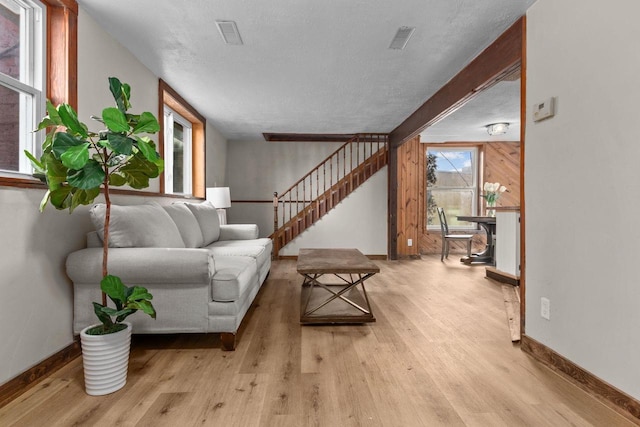 living room featuring a textured ceiling, wooden walls, light hardwood / wood-style flooring, and a healthy amount of sunlight