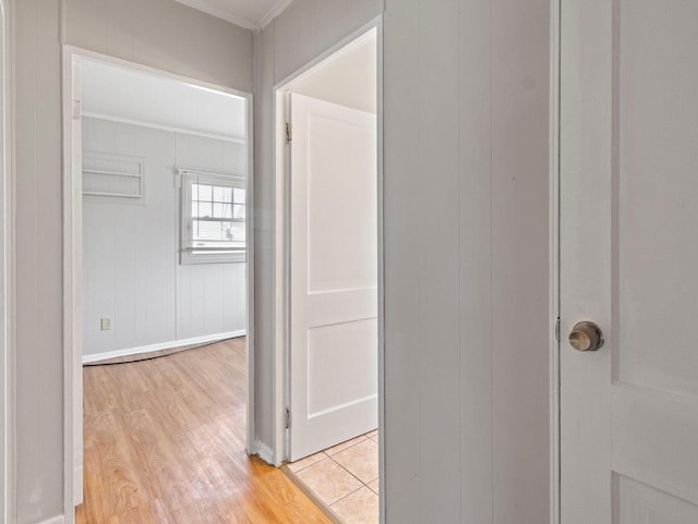 corridor with wood walls, ornamental molding, and light wood-type flooring