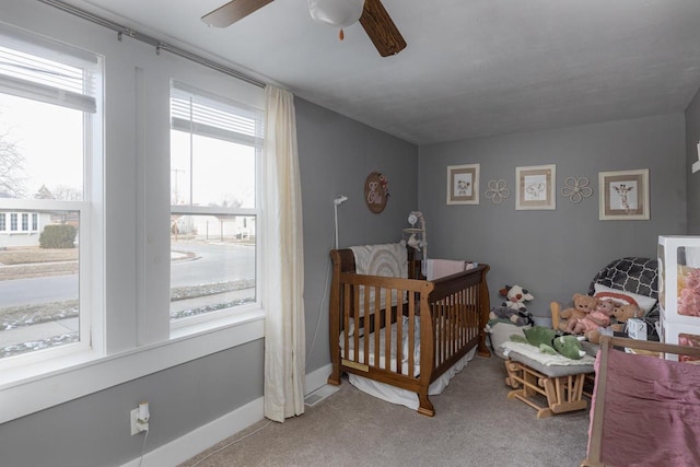 carpeted bedroom featuring multiple windows, ceiling fan, and a nursery area