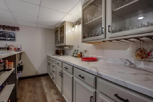 interior space with a paneled ceiling, light stone countertops, dark hardwood / wood-style flooring, and sink