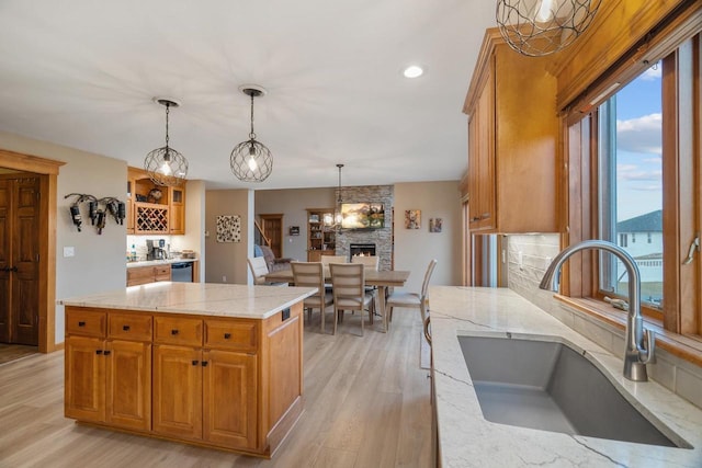 kitchen with light stone countertops, light wood-type flooring, sink, a center island, and hanging light fixtures