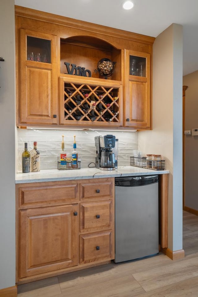 bar with stainless steel dishwasher, light hardwood / wood-style flooring, and tasteful backsplash