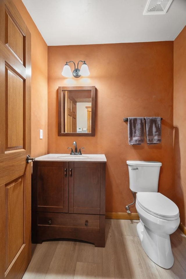 bathroom with visible vents, baseboards, toilet, wood finished floors, and vanity