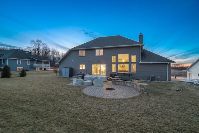 rear view of house featuring a hot tub, an outdoor living space with a fire pit, a lawn, a chimney, and a patio