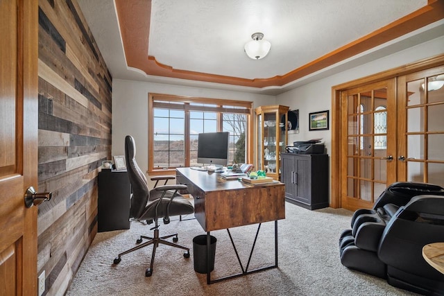 carpeted office featuring a raised ceiling, french doors, and wood walls