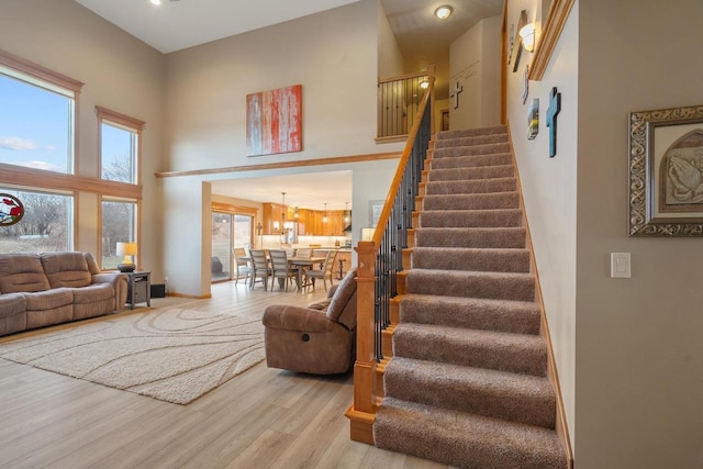 stairway featuring wood-type flooring, an inviting chandelier, a wealth of natural light, and a high ceiling