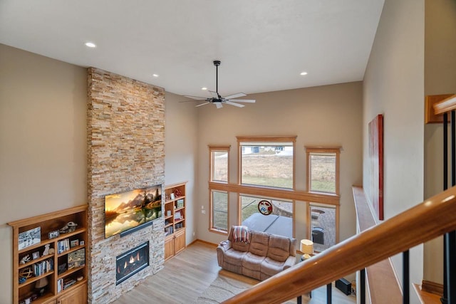 living room featuring light wood-type flooring, a stone fireplace, and ceiling fan