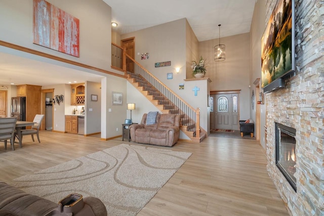 living area with baseboards, stairway, a stone fireplace, light wood-style flooring, and a towering ceiling