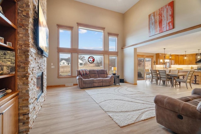 living room with a wealth of natural light, a stone fireplace, light wood-style flooring, and a high ceiling