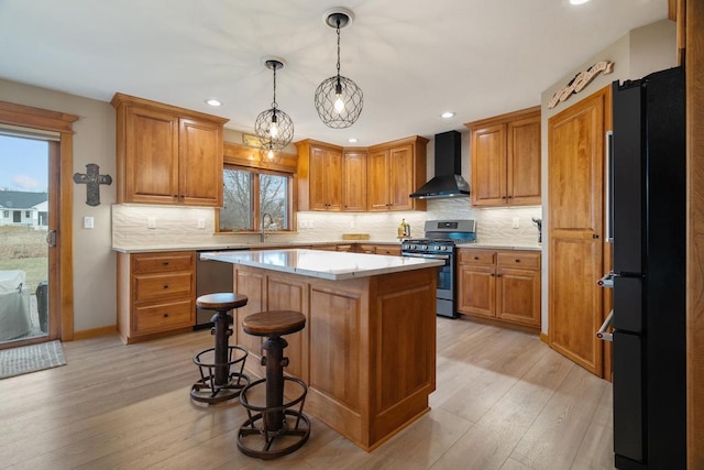 kitchen with a center island, stainless steel appliances, wall chimney exhaust hood, brown cabinetry, and light countertops