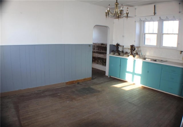 kitchen with blue cabinetry, sink, dark hardwood / wood-style flooring, a notable chandelier, and wooden walls