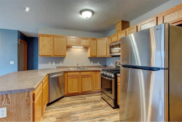 kitchen with sink, light hardwood / wood-style flooring, a textured ceiling, appliances with stainless steel finishes, and kitchen peninsula