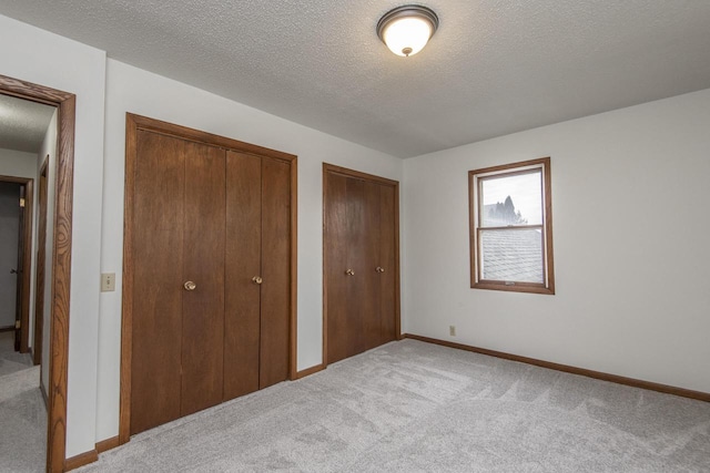 unfurnished bedroom featuring light carpet, a textured ceiling, and multiple closets