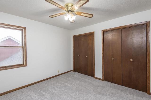 unfurnished bedroom featuring ceiling fan, light colored carpet, a textured ceiling, and two closets