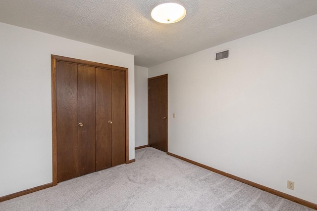 unfurnished bedroom with light carpet, a closet, and a textured ceiling