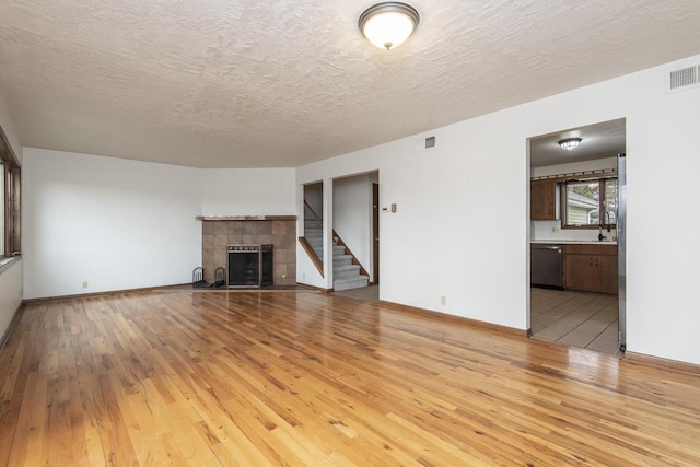 unfurnished living room with a textured ceiling, sink, a fireplace, and light hardwood / wood-style flooring