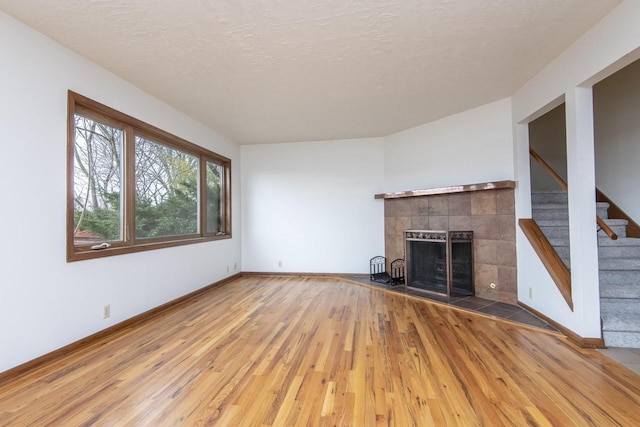 unfurnished living room featuring hardwood / wood-style flooring, a textured ceiling, and a tiled fireplace