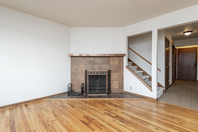 unfurnished living room with a tiled fireplace and wood-type flooring