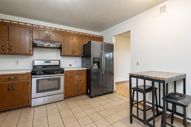 kitchen featuring a kitchen bar, exhaust hood, light tile patterned flooring, and stainless steel appliances