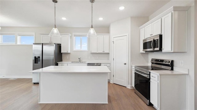 kitchen with hanging light fixtures, appliances with stainless steel finishes, white cabinetry, and a kitchen island