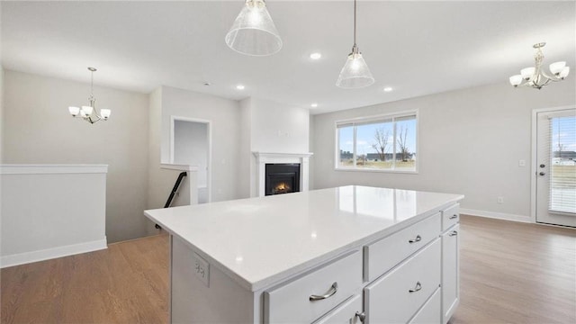 kitchen featuring pendant lighting, light hardwood / wood-style floors, a center island, white cabinets, and a chandelier