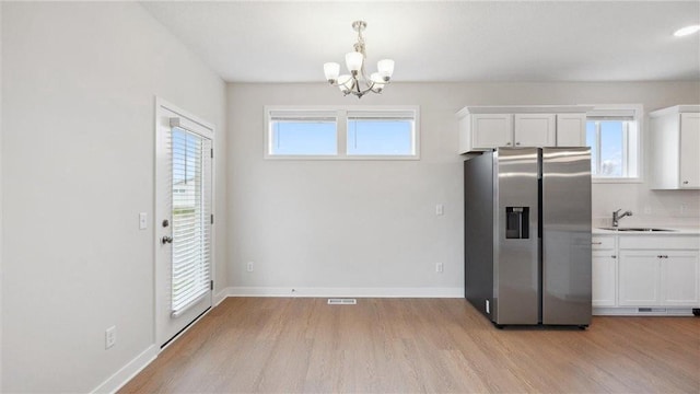 kitchen featuring white cabinets, light hardwood / wood-style floors, sink, stainless steel fridge, and a chandelier