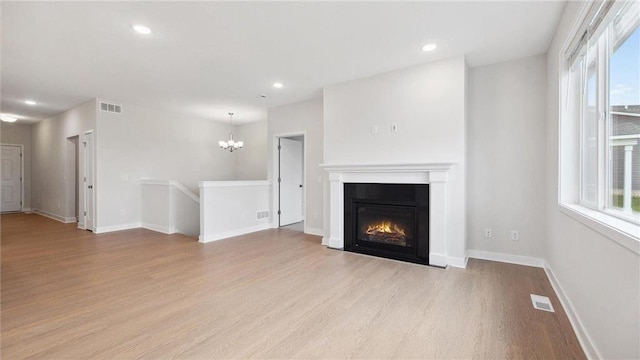 unfurnished living room with an inviting chandelier and light hardwood / wood-style flooring