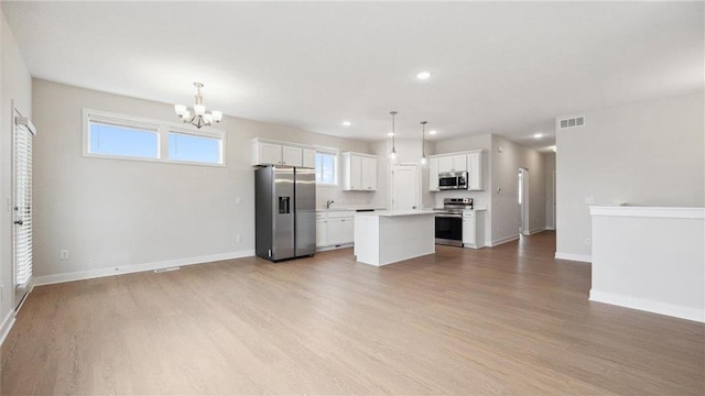 kitchen with white cabinetry, appliances with stainless steel finishes, hanging light fixtures, a kitchen island, and light hardwood / wood-style flooring