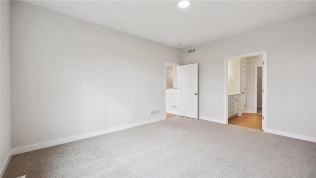 unfurnished bedroom featuring connected bathroom and light carpet