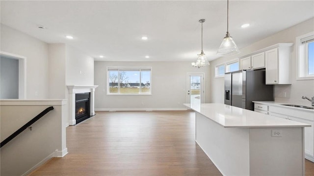 kitchen with white cabinets, a kitchen island, decorative light fixtures, sink, and stainless steel fridge