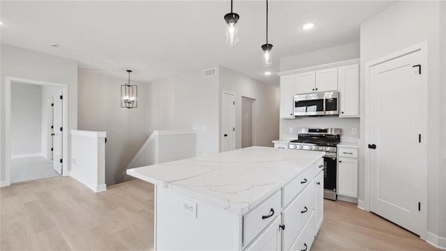 kitchen with stainless steel appliances, pendant lighting, white cabinetry, light hardwood / wood-style flooring, and a kitchen island