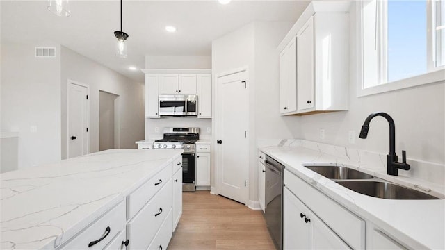 kitchen with appliances with stainless steel finishes, light stone counters, sink, white cabinets, and hanging light fixtures